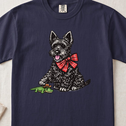 Navy blue t-shirt featuring an illustration of a black terrier wearing a red plaid bow tie, touching a toy alligator.