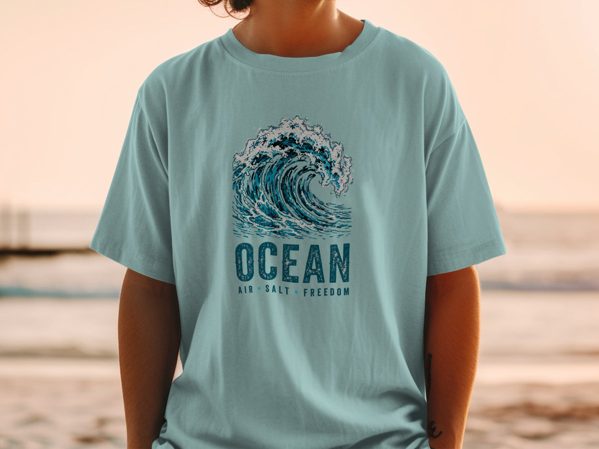 Light blue t-shirt with a large wave graphic and text "OCEAN AIR SALT FREEDOM".
