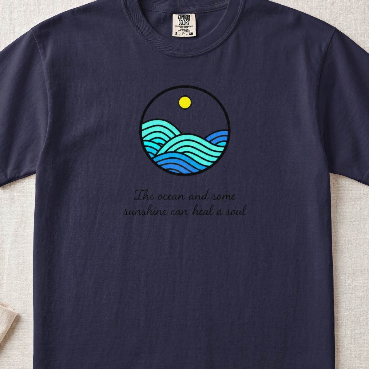 A dark navy t-shirt featuring a circular ocean graphic and the text The ocean and some sunshine can heal a soul.