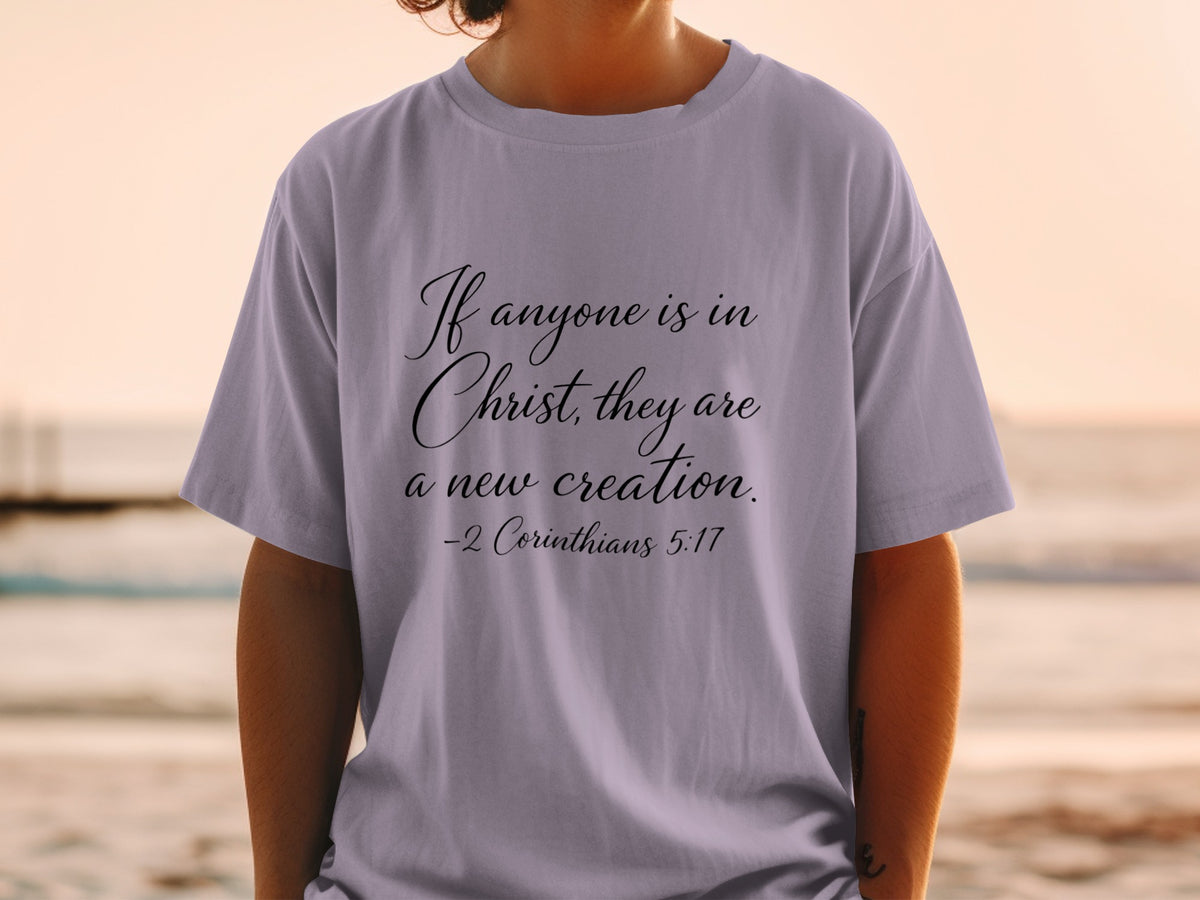Lavender t-shirt with black script text: "If anyone is in Christ, they are a new creation. -2 Corinthians 5:17"