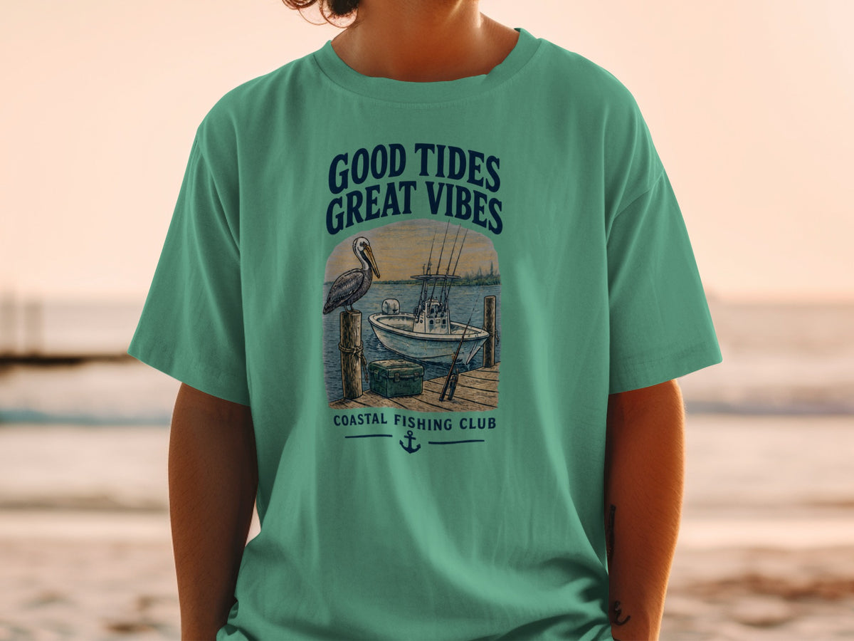 T-shirt graphic with pelican, boat, fishing rods, and text "GOOD TIDES GREAT VIBES COASTAL FISHING CLUB".