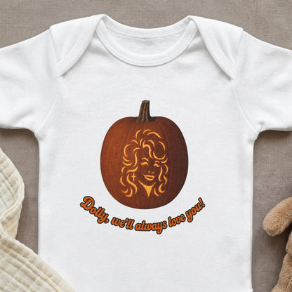 White baby onesie with a carved pumpkin featuring Dolly Parton's face and text "Dolly, we'll always love you!".
