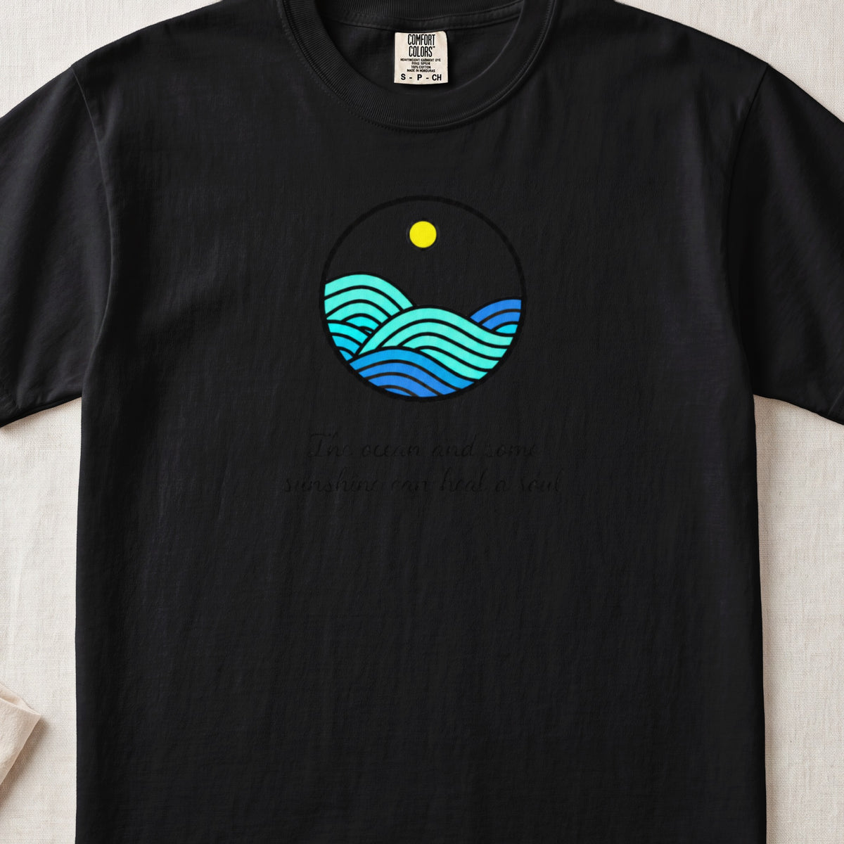 Black t-shirt featuring a circular graphic of blue ocean waves under a yellow sun and text.