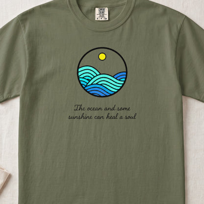 An olive green t-shirt with a round graphic of ocean waves and text reading The ocean and some sunshine can heal a soul.