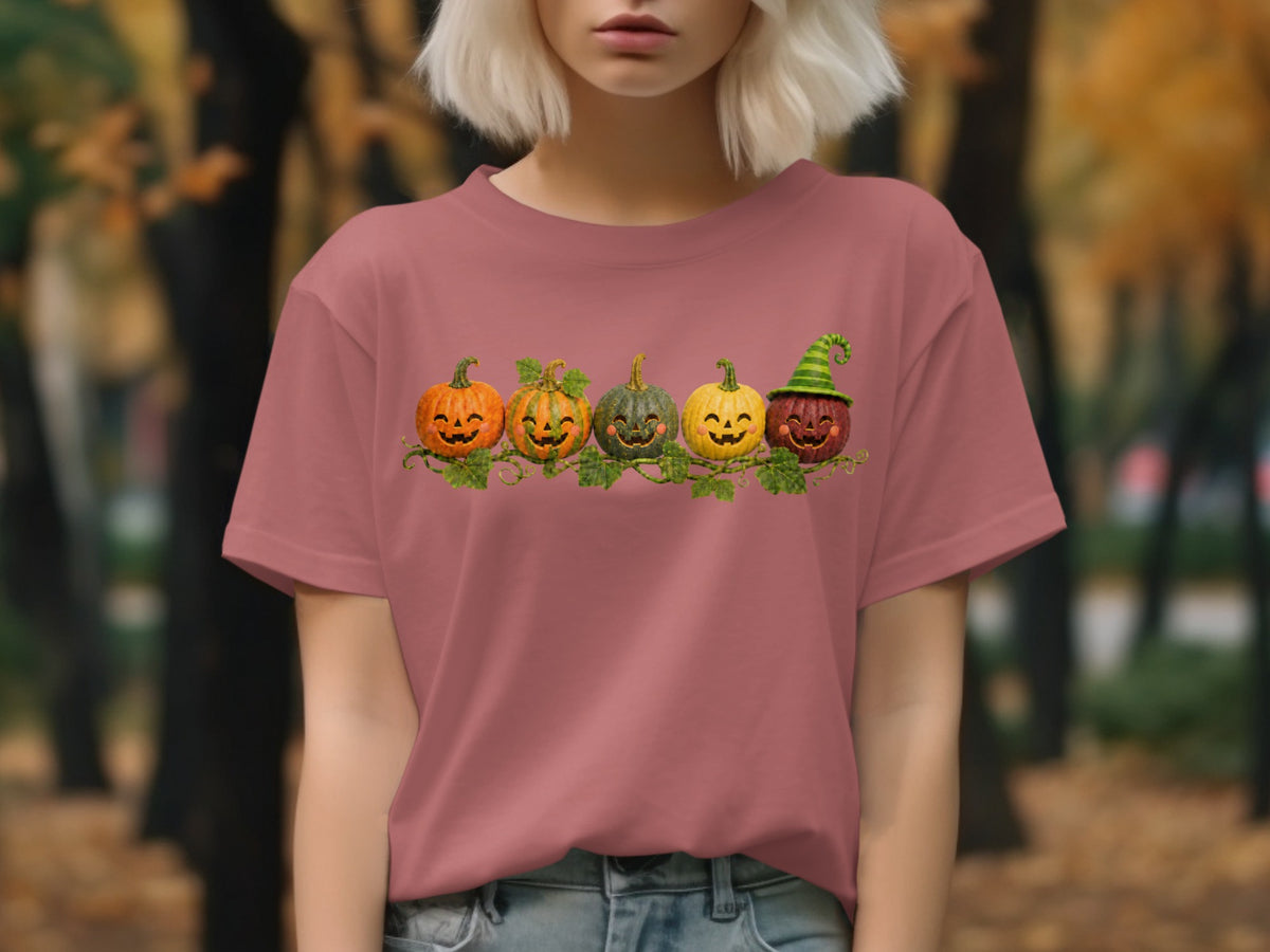 Five jack-o'-lanterns with cheerful faces on a vine across a pink t-shirt.