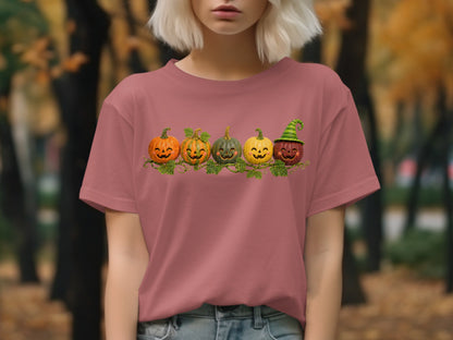 Five jack-o'-lanterns with cheerful faces on a vine across a pink t-shirt.