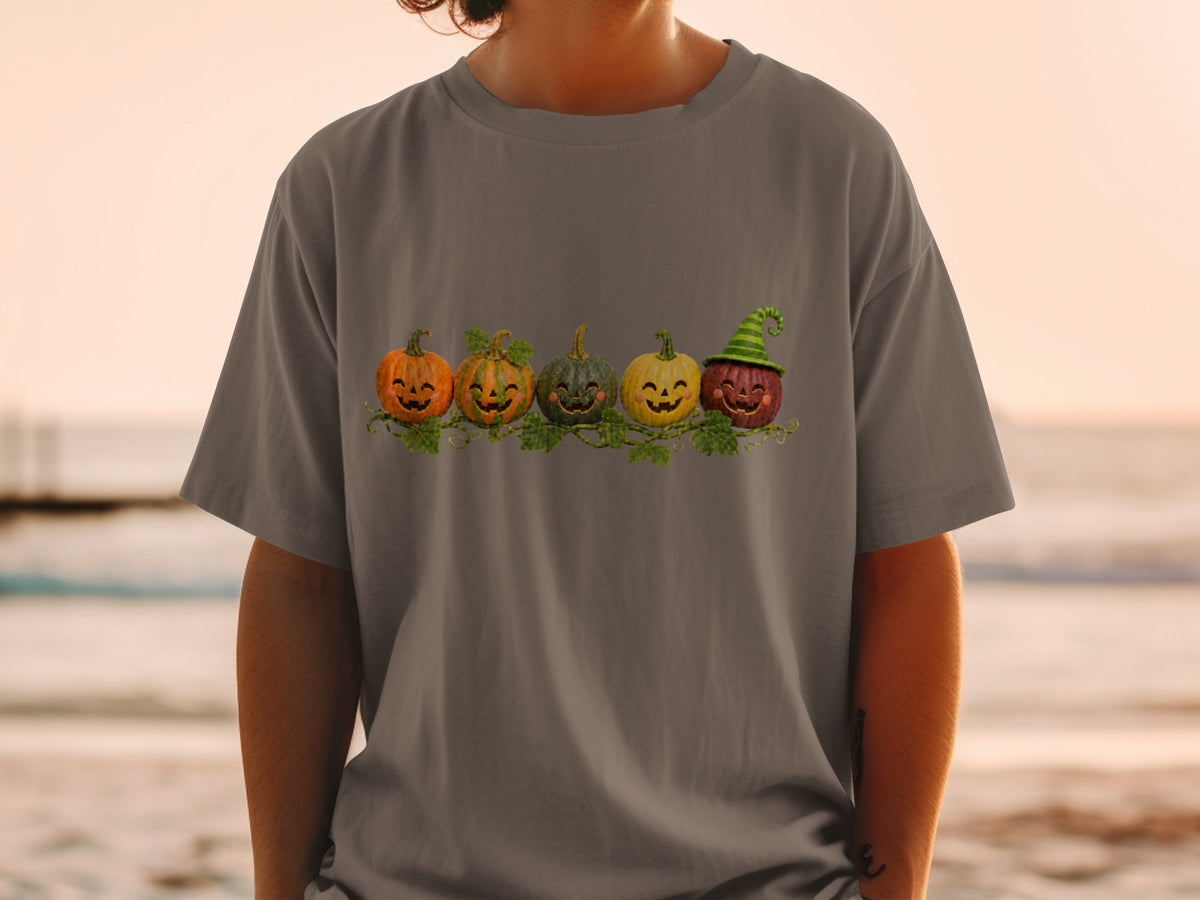 Five smiling cartoon pumpkins with vines adorn a grey t-shirt.