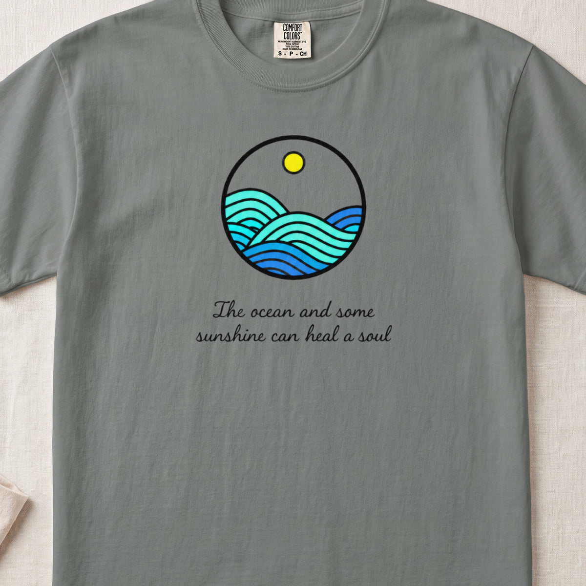 A grey t-shirt featuring a circular ocean and sun graphic with text below it.