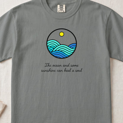 A grey t-shirt featuring a circular ocean and sun graphic with text below it.