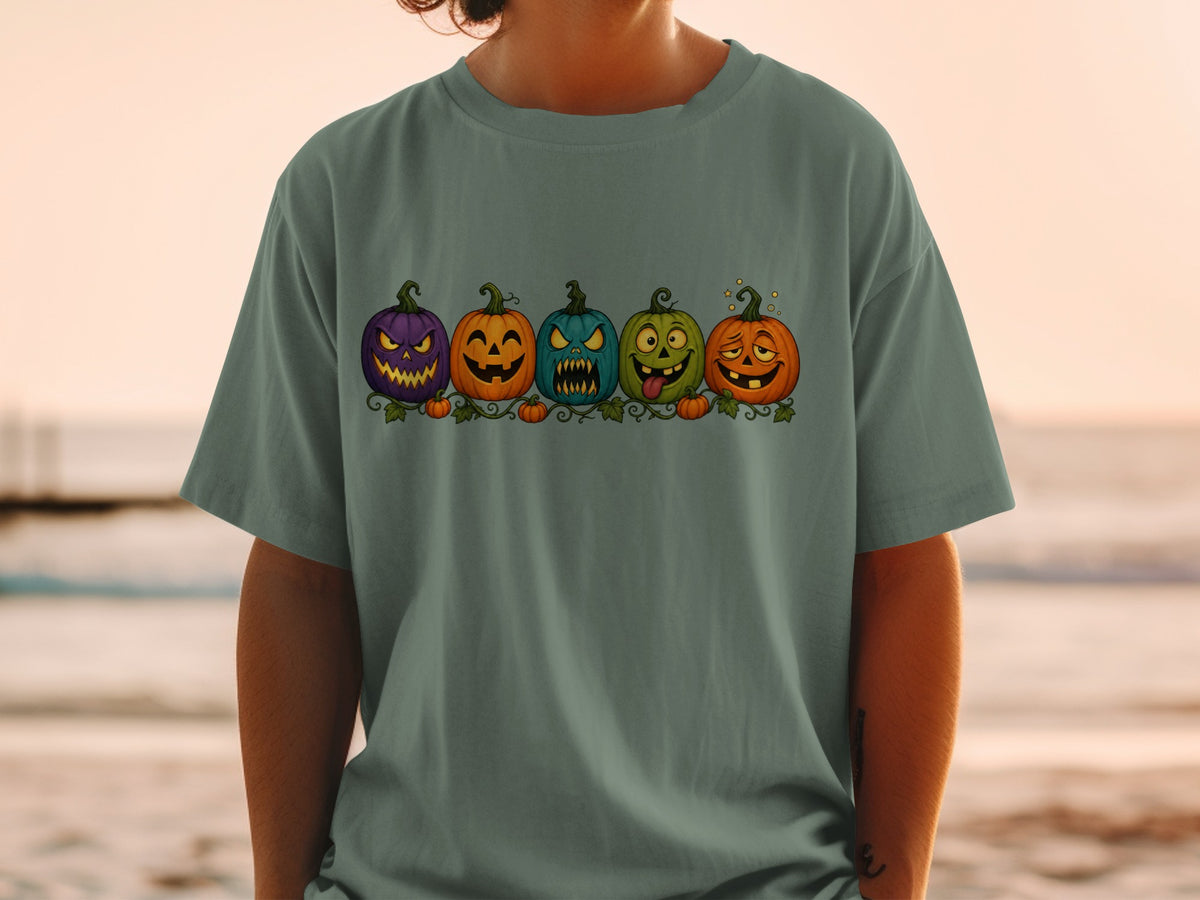 Five cartoon jack-o'-lanterns with different spooky faces on a green t-shirt.