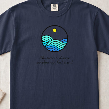 Dark navy t-shirt featuring a circular ocean graphic with a yellow sun and text reading The ocean and some sunshine can heal a soul.