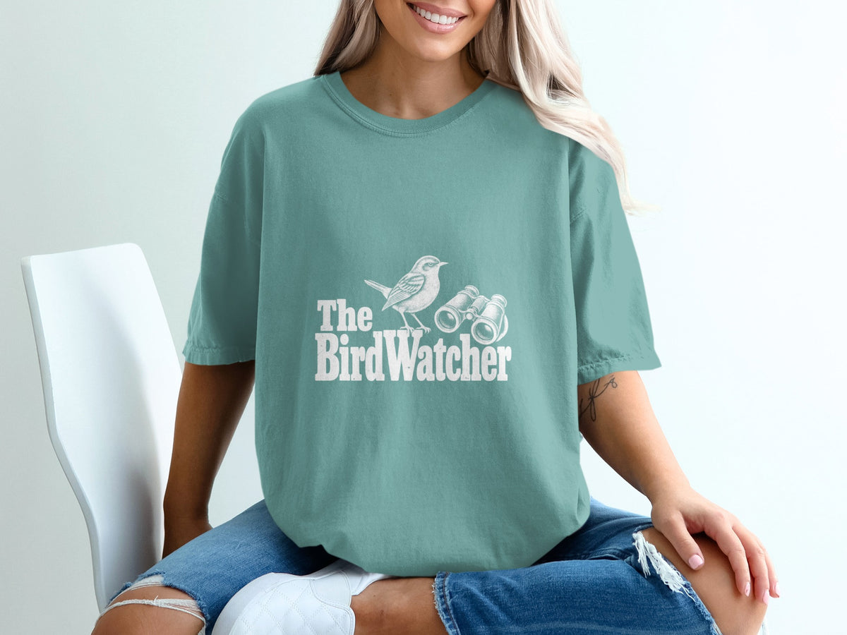 Teal t-shirt with white text "The BirdWatcher" and graphics of a bird and binoculars.