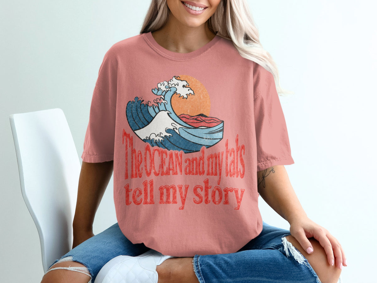 Coral t-shirt with a graphic of a wave, sun, and text: "The OCEAN and my tats tell my story".