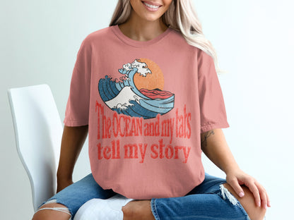 Coral t-shirt with a graphic of a wave, sun, and text: "The OCEAN and my tats tell my story".