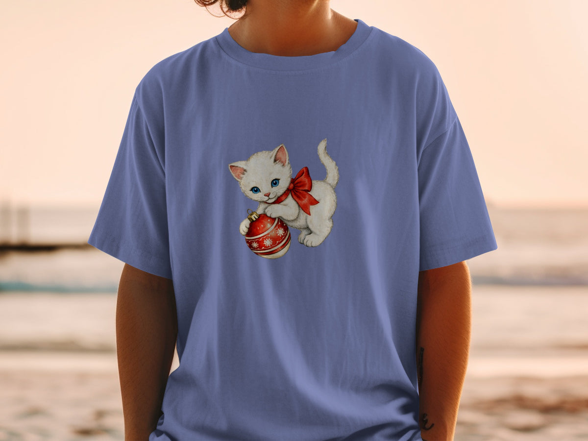 White kitten with blue eyes and red bow holding a red ornament.