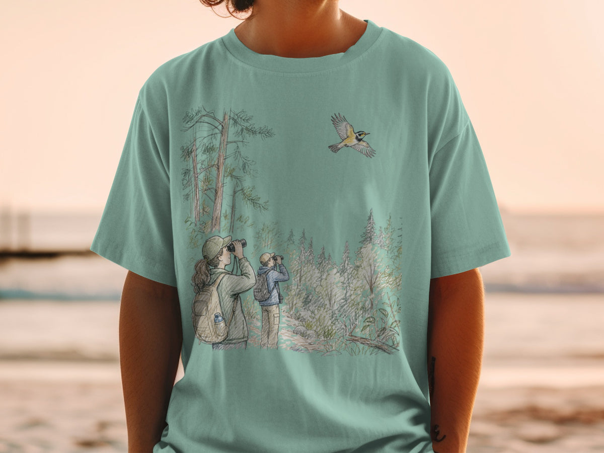 Two birdwatchers observe a bird flying over a forest landscape on a teal t-shirt.