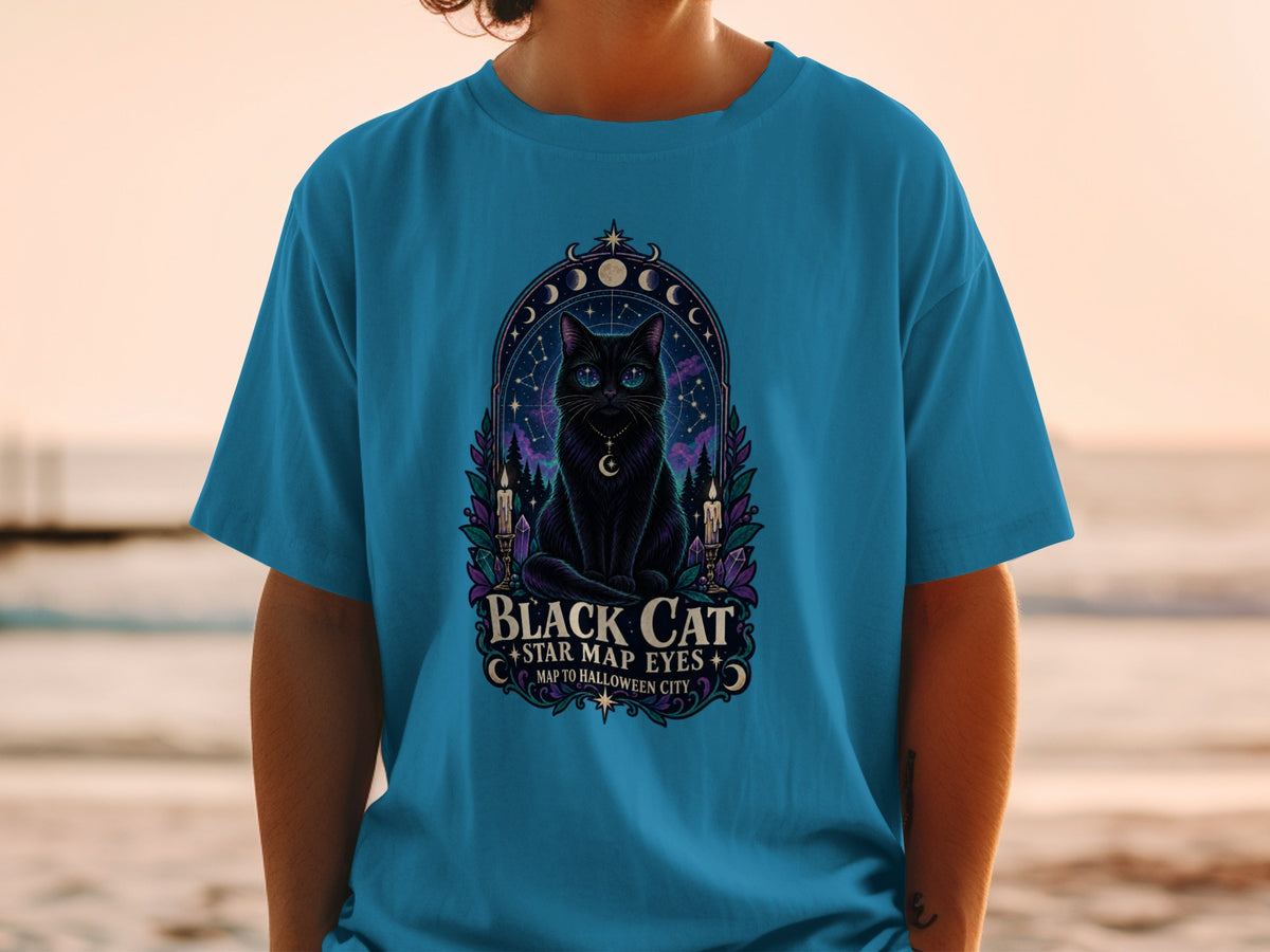 Black cat with star map eyes and celestial elements on a teal t-shirt.