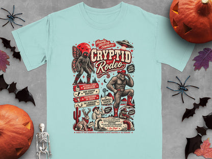 Light blue t-shirt with Cryptid Rodeo graphic featuring Bigfoot, Mothman, and other mythical creatures.