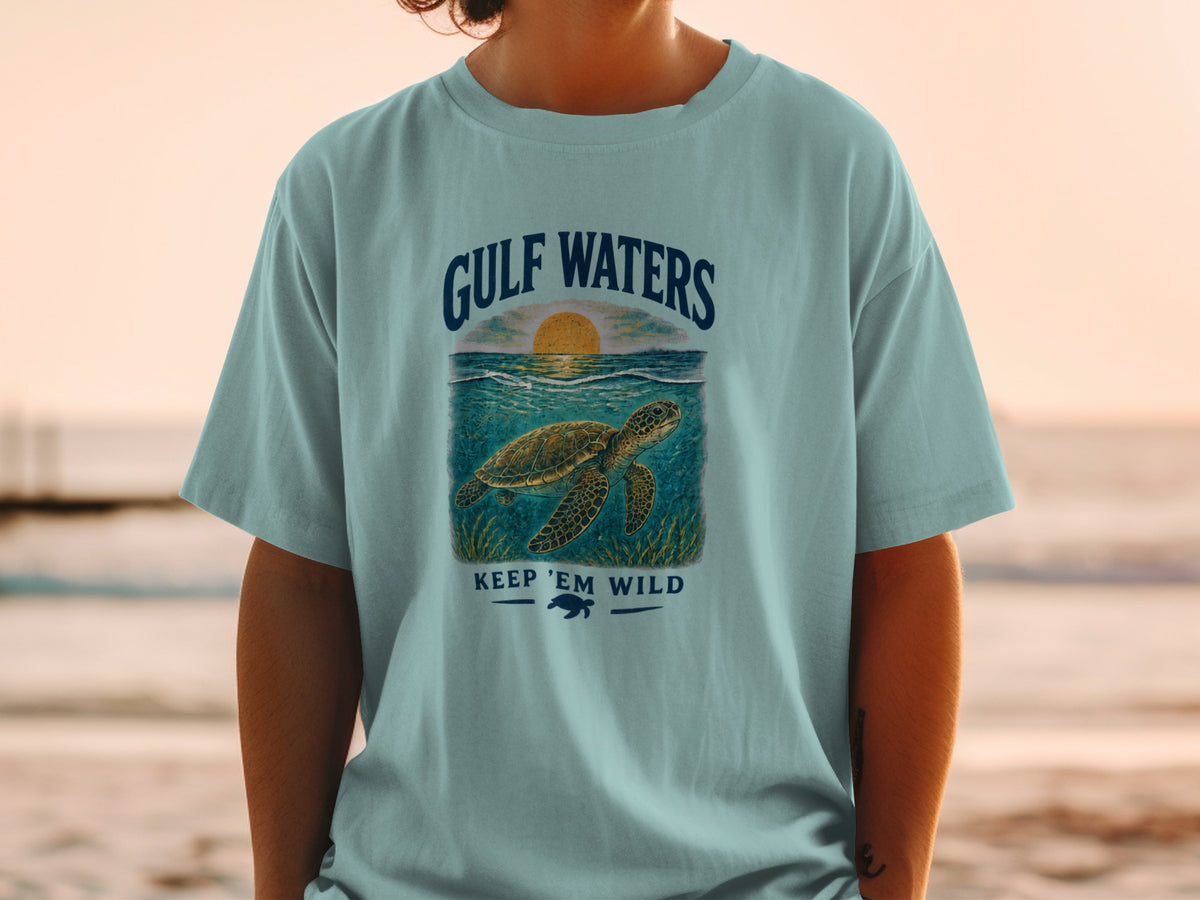 Light blue t-shirt with a graphic of a sea turtle, sunset, and text "GULF WATERS KEEP 'EM WILD".