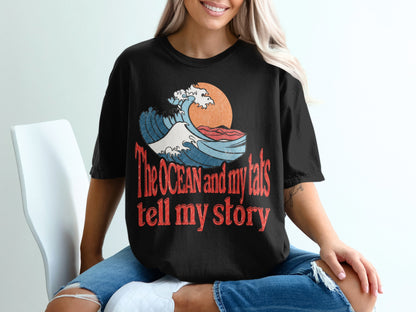 Black t-shirt with graphic of wave, sun, and text "The ocean and my tats tell my story".