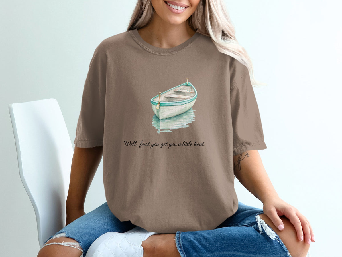 Brown t-shirt with watercolor boat graphic and "Well, first you get you a little boat" text.