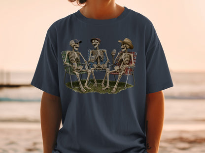 Three skeletons sit in lawn chairs on grass, holding drinks.