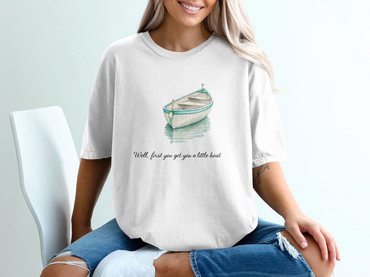 White t-shirt with a watercolor painting of a rowboat and text reading "Well, first you get you a little boat".