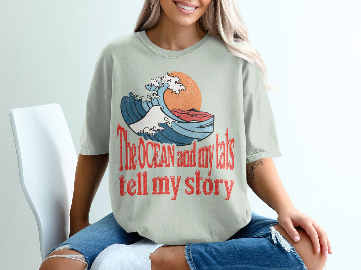 T-shirt with graphic of wave and sun, text "The OCEAN and my tats tell my story".