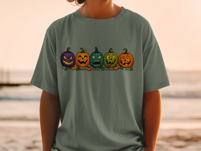 Five cartoon Halloween pumpkins with expressive faces on a dark green t-shirt.