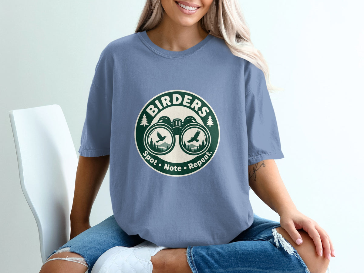 T-shirt with round graphic featuring binoculars, birds, trees, and text "Birders Spot Note Repeat."