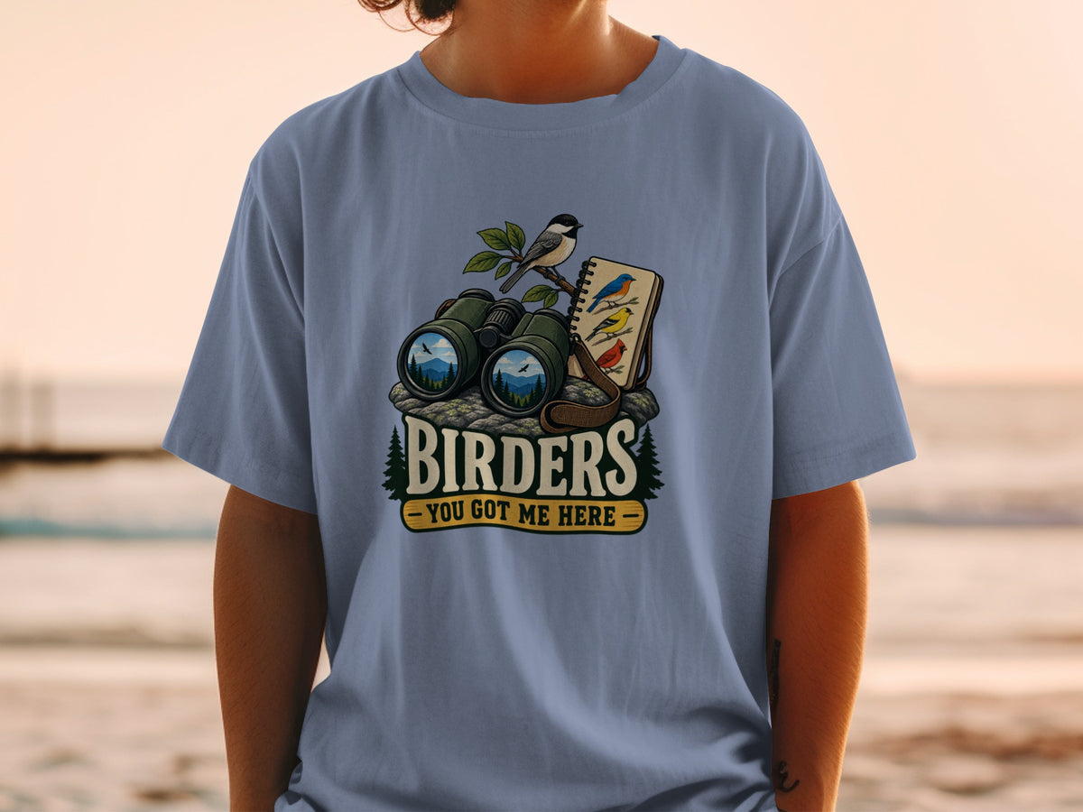Binoculars, bird, and notebook on rocks with text "BIRDERS YOU GOT ME HERE".