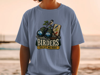 Binoculars, bird, and notebook on rocks with text "BIRDERS YOU GOT ME HERE".