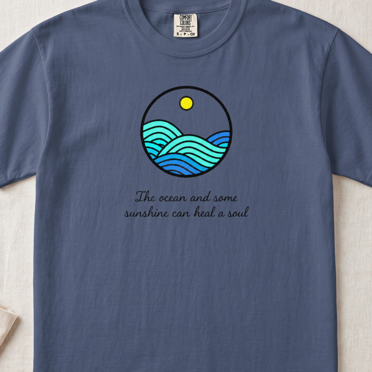 A blue t-shirt featuring a circular ocean graphic and the text The ocean and some sunshine can heal a soul.