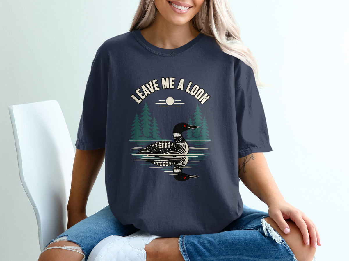 T-shirt with graphic of loon on water, trees, and text "LEAVE ME A LOON".