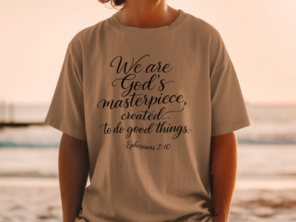 Tan t-shirt with black text "We are God's masterpiece, created... to do good things. -Ephesians 2:10".