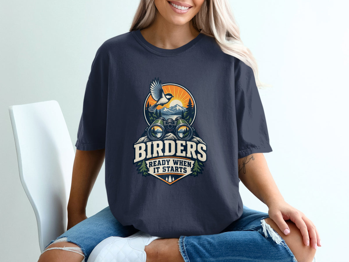 Dark blue t-shirt graphic with binoculars, bird, mountains, and text "BIRDERS READY WHEN IT STARTS".