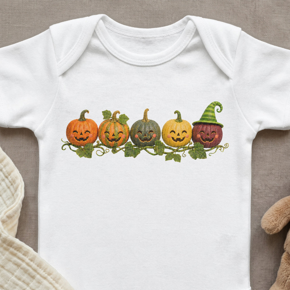 White baby bodysuit with a row of smiling jack-o'-lanterns and a witch hat.