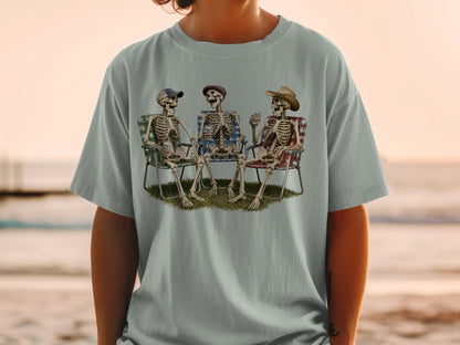 Three skeletons sitting in beach chairs on grass with drinks.