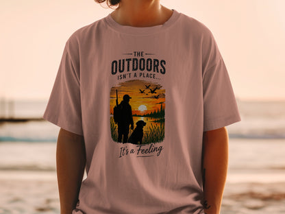 T-shirt graphic: hunter, dog, sunset, and text "The outdoors isn't a place... It's a feeling."