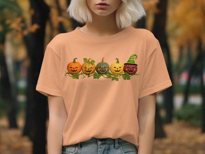 Peach t-shirt with a graphic of five smiling pumpkins and green vines.