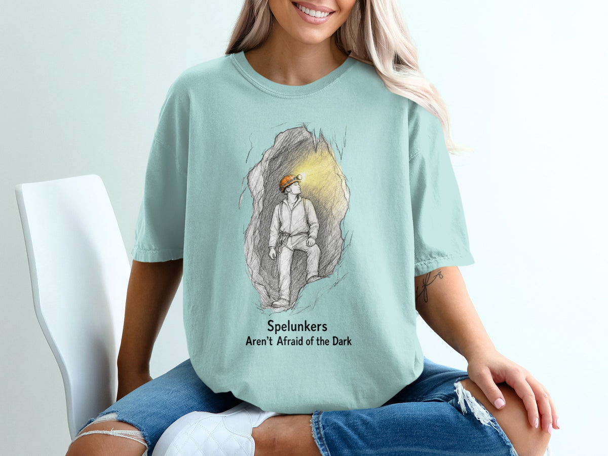Pale blue t-shirt with illustration of spelunker in cave and text "Spelunkers Aren't Afraid of the Dark".