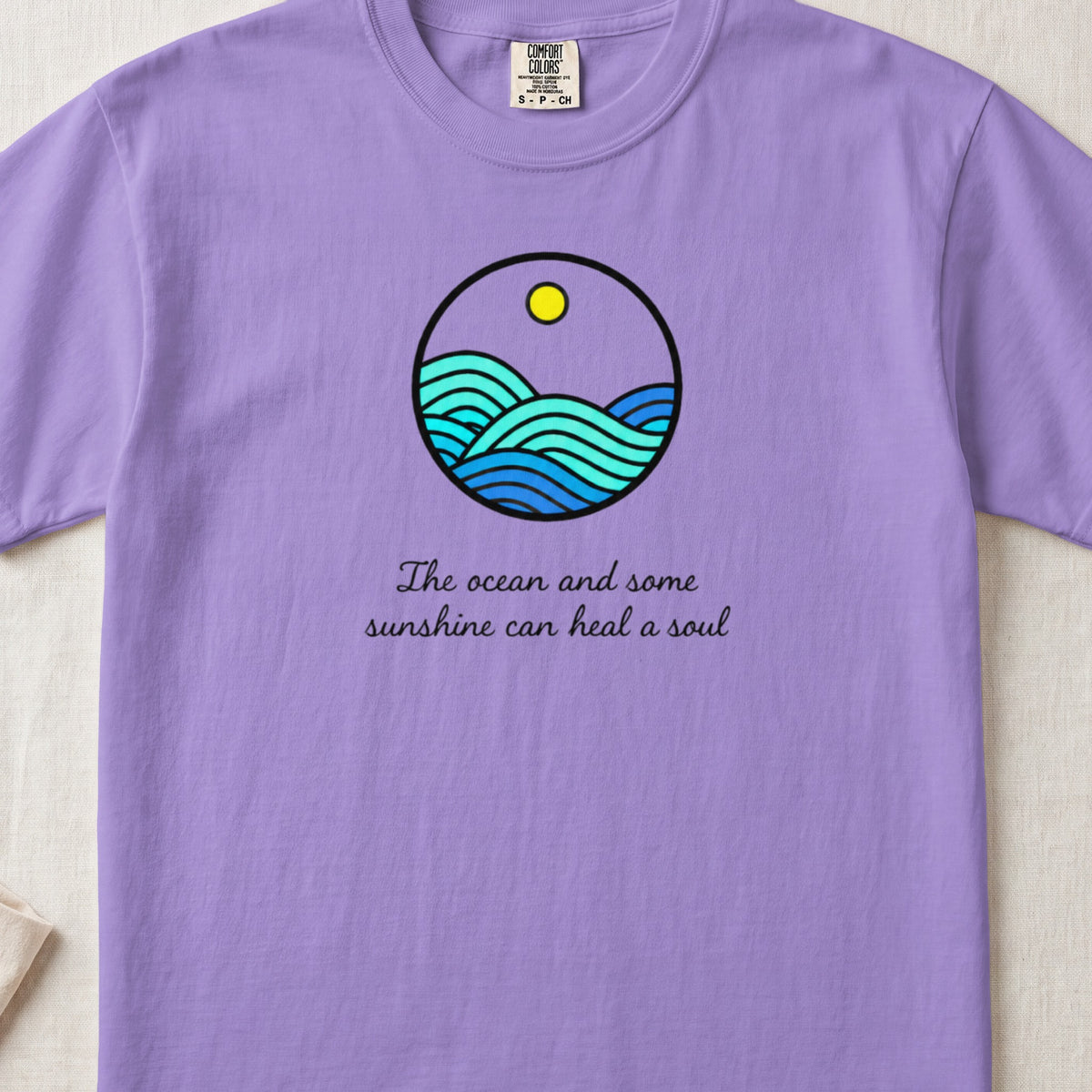 Purple t-shirt with a circular ocean waves graphic and "The ocean and some sunshine can heal a soul" text.