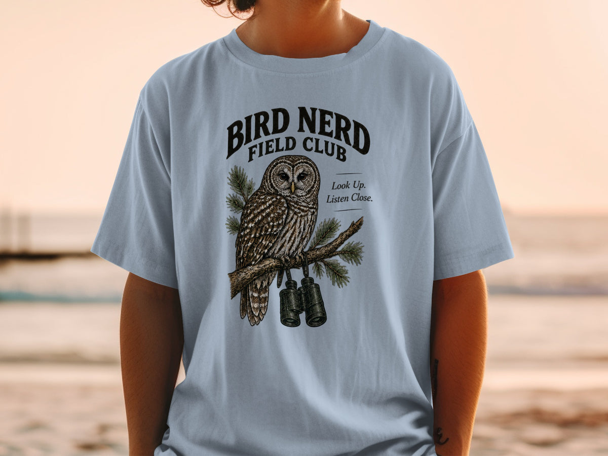 Light blue t-shirt with "BIRD NERD FIELD CLUB" text and owl graphic with binoculars.