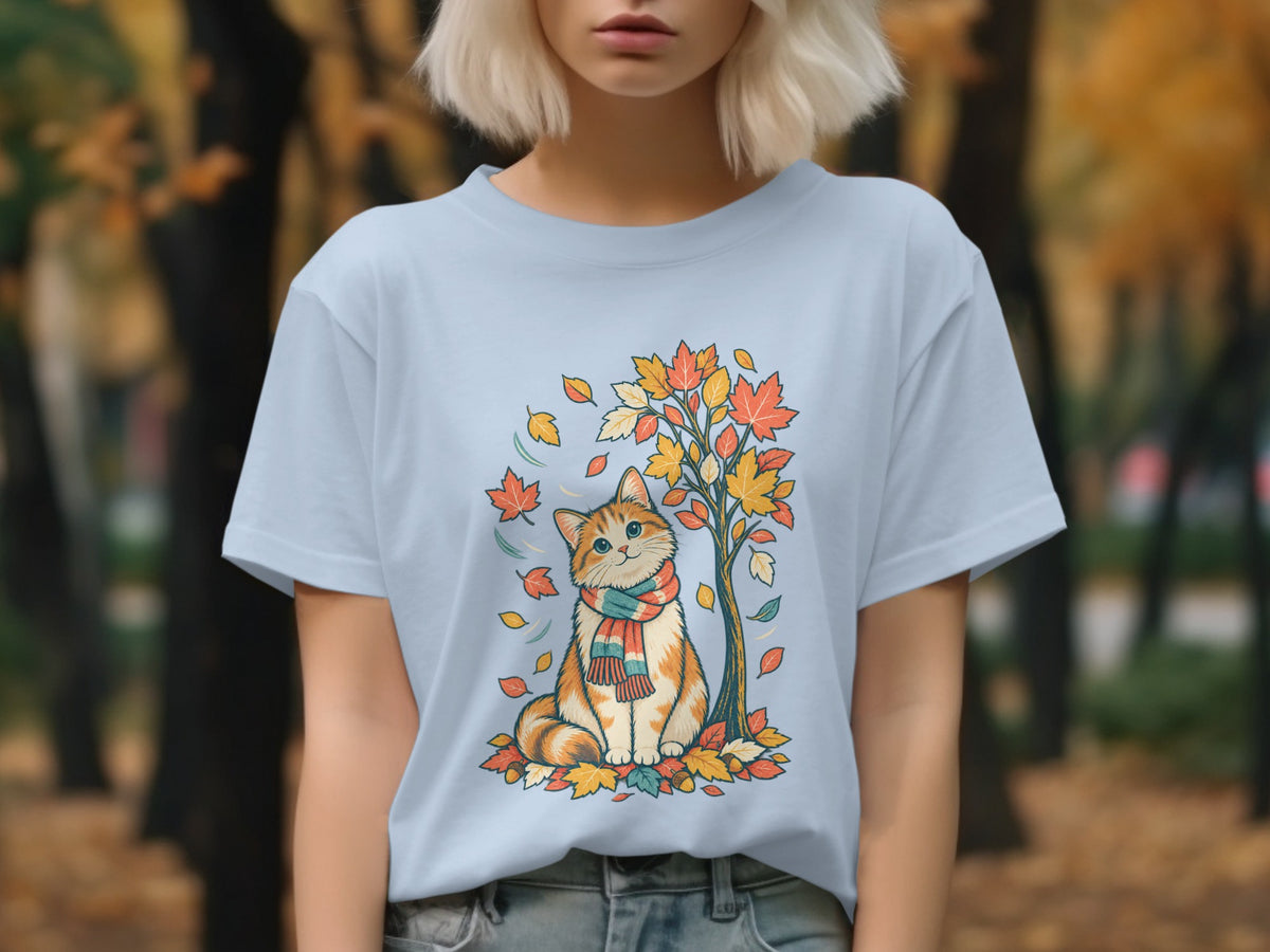 Light blue t-shirt with a cartoon cat in a scarf sitting by a fall tree.