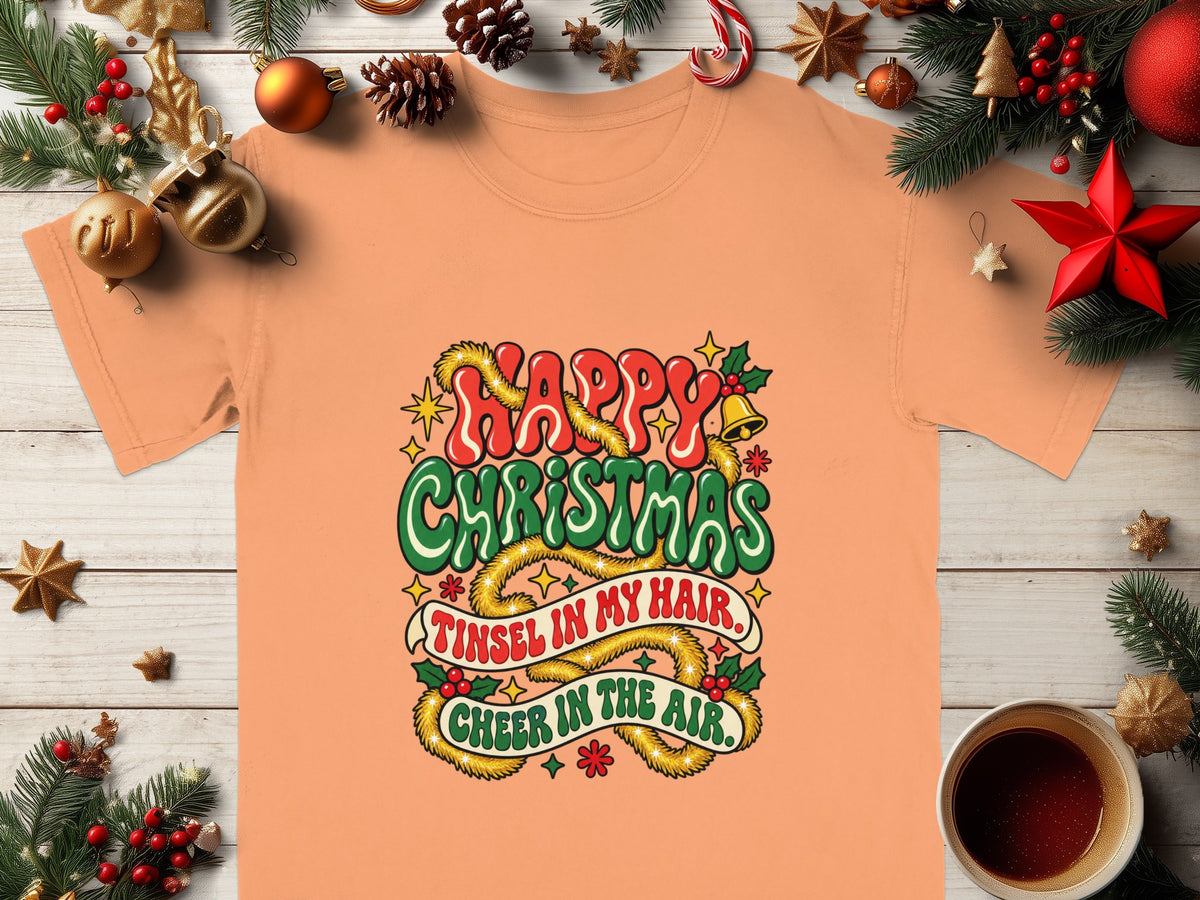 Peach t-shirt with "Happy Christmas" and "Tinsel in My Hair. Cheer in the Air." text.