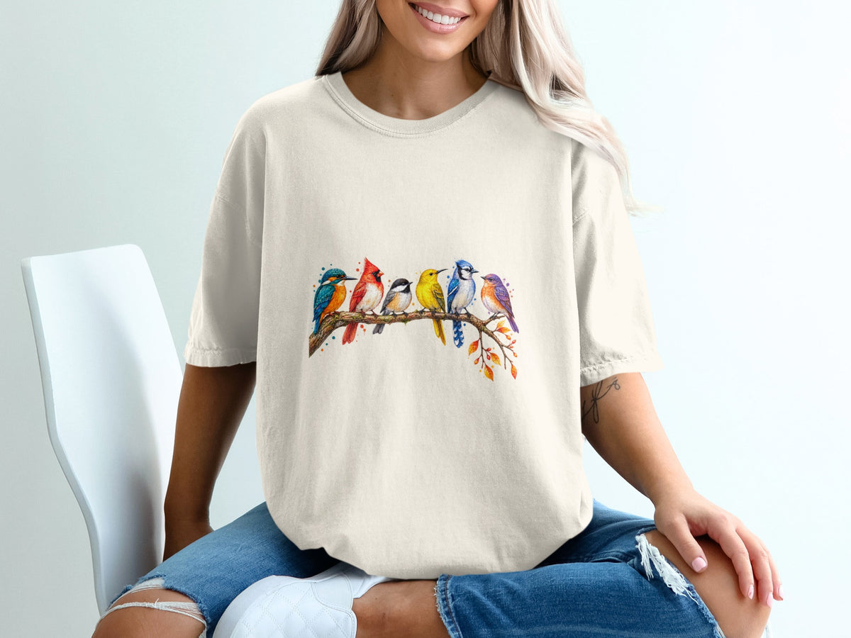 Beige t-shirt with a watercolor illustration of seven colorful birds perched on a branch.