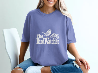 Purple t-shirt with white graphic of a bird and binoculars that reads "The Bird Watcher".