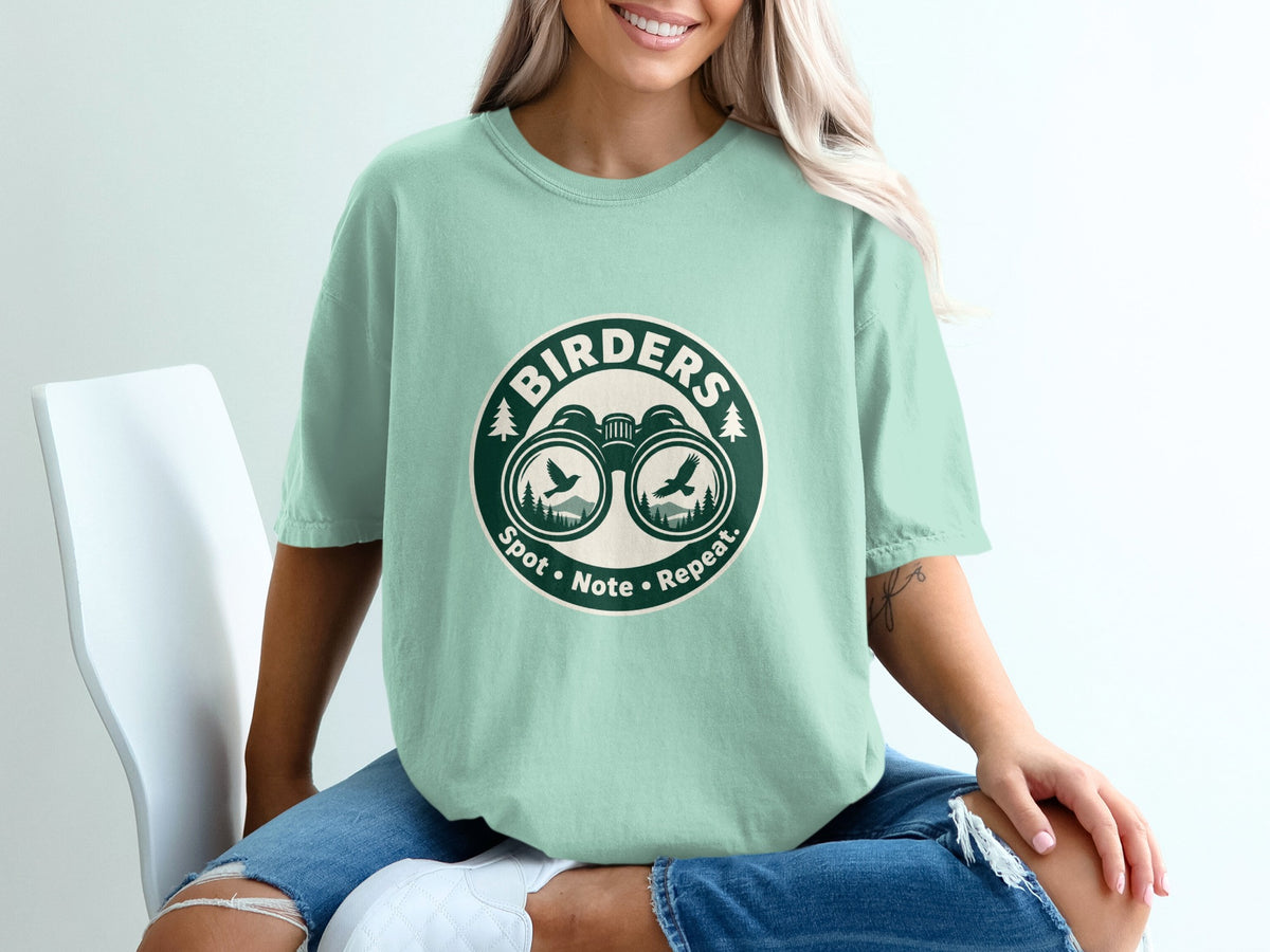 Mint green t-shirt with circular graphic of binoculars, birds, trees, and text "Birders Spot Note Repeat."