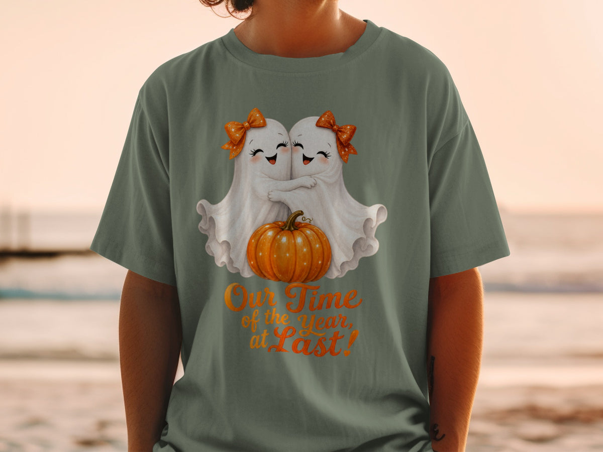 Two ghosts hug a pumpkin on a t-shirt with text "Our Time of the Year, at Last!".