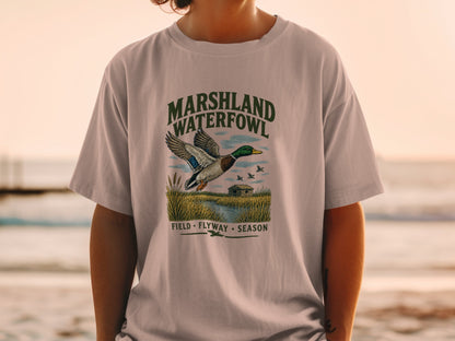 T-shirt graphic with mallard duck flying over marshland, "MARSHLAND WATERFOWL" text.